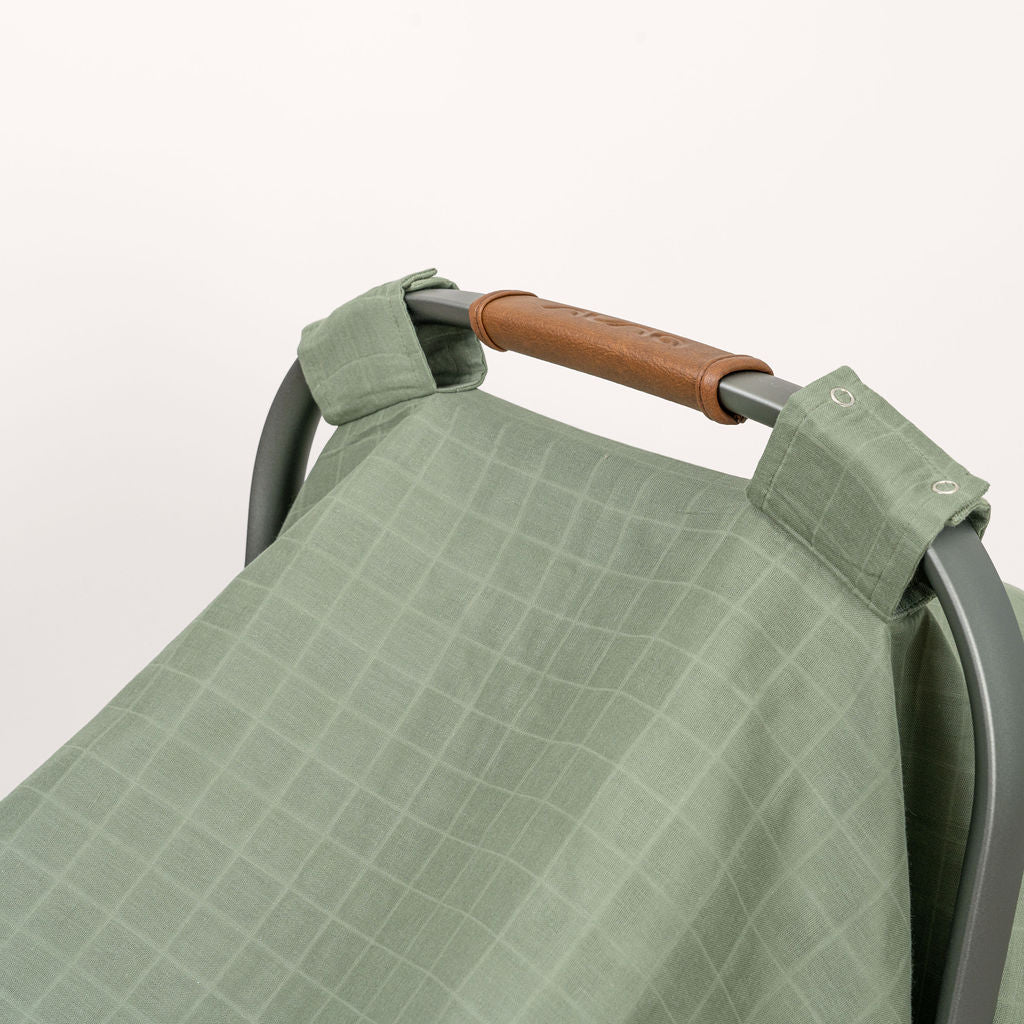 Green muslin car seat cover with buttoned strap and folded corner detail