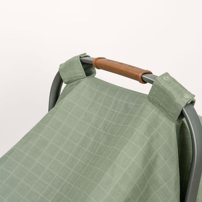 Green muslin car seat cover with buttoned strap and folded corner detail