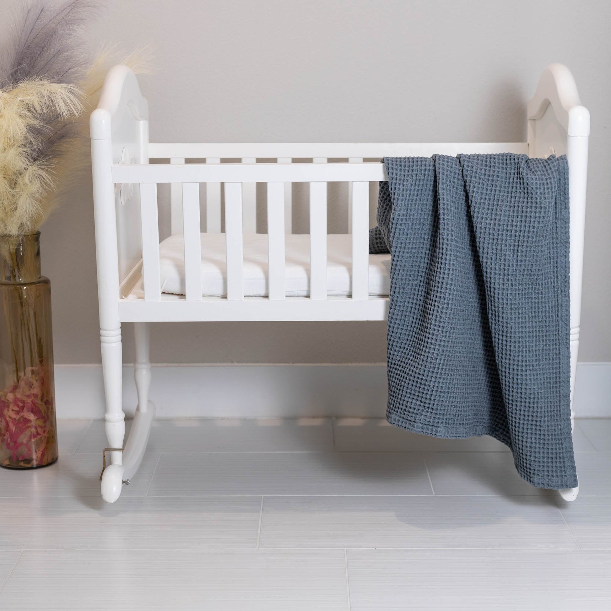 Waffle baby blanket in blue, draped over a crib and folded in waffle texture