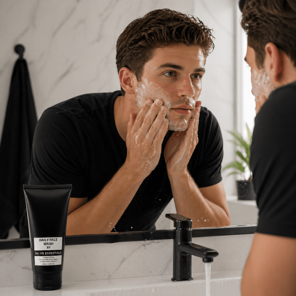 Dark face wash tube beside sink as man washes face with foam