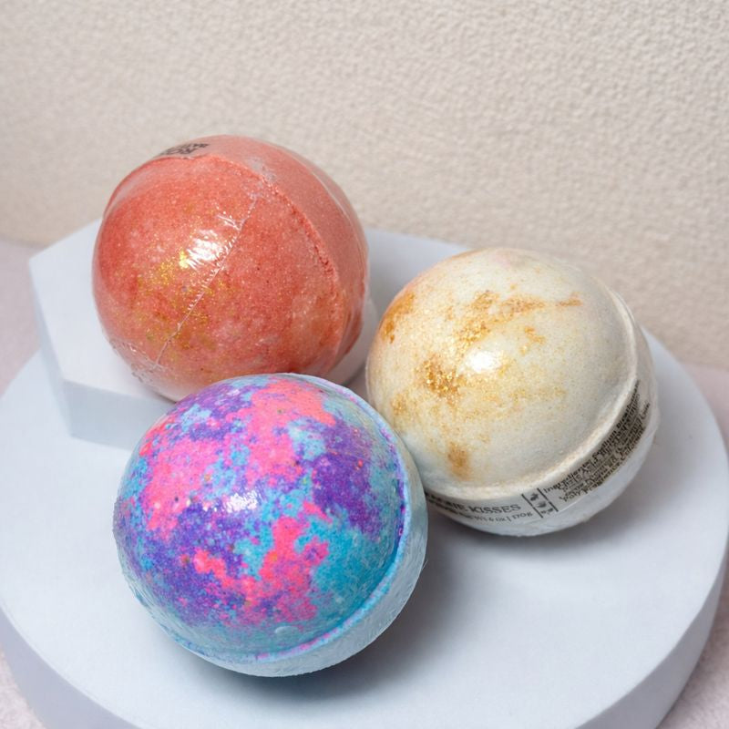 Bath bomb box with red, blue-speckled, and cream spherical bath bombs on white risers