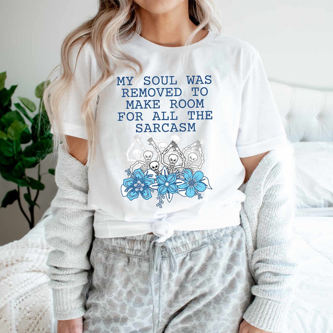 White short-sleeve T-shirt with blue slogan text and skull-and-flower graphic
