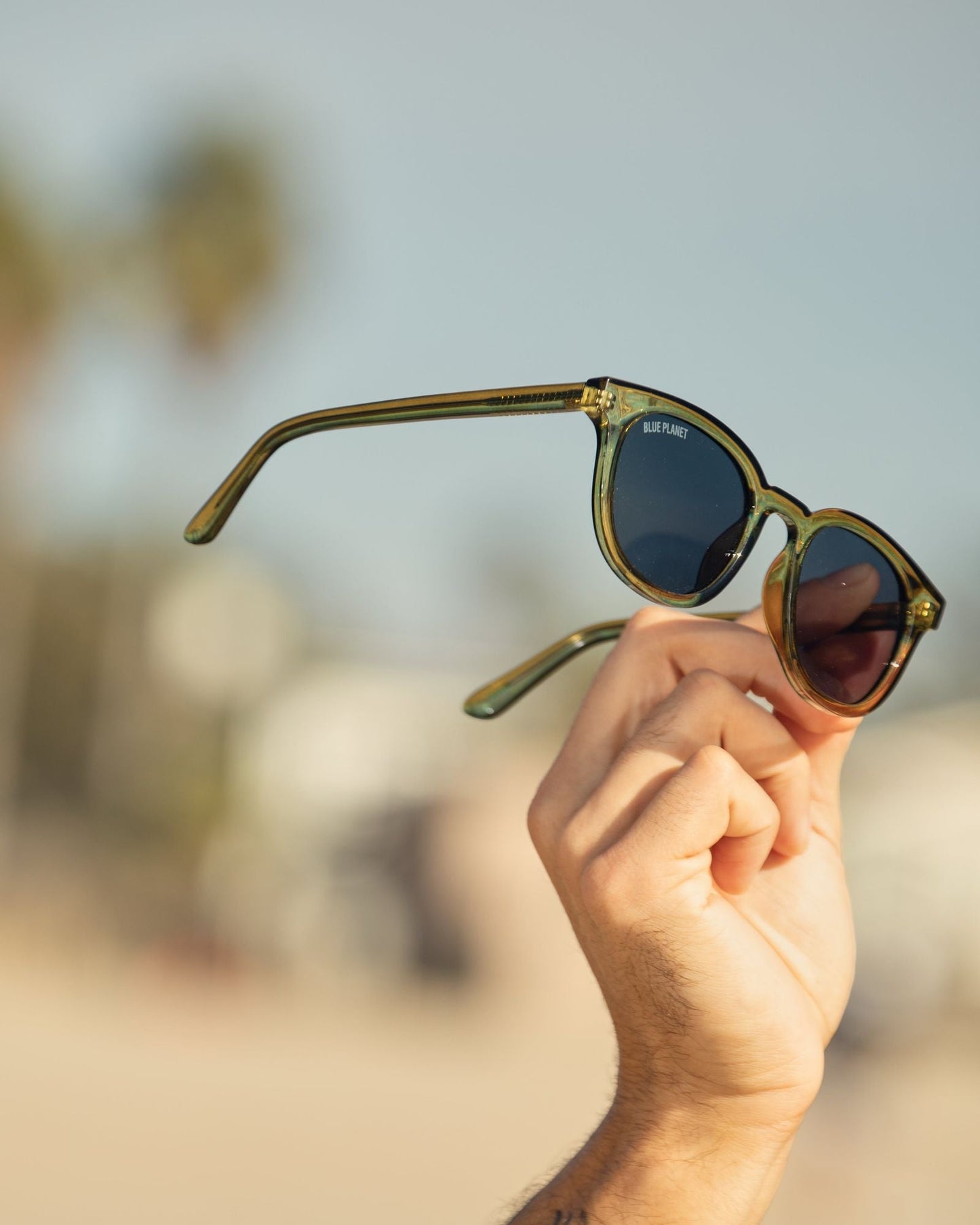 Olive green polarized sunglasses held in hand, dark round lenses