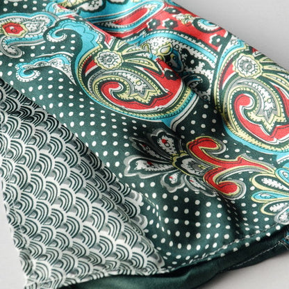 Close-up of teal-green silk scarf fabric with paisley, swirls, and white dot details.