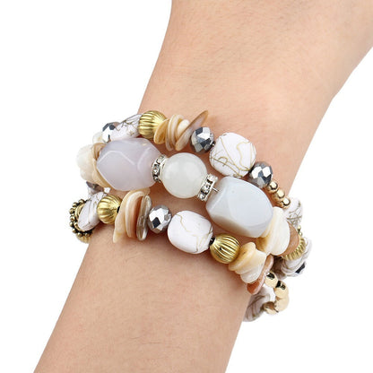 Multilayer charm bracelet on wrist with white oval beads, black crystal accents, and gold spacers