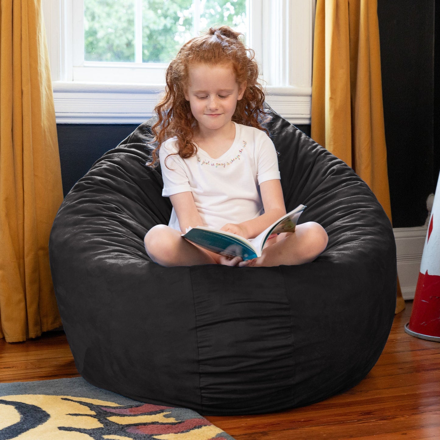 Black kids cocoon bean bag with microsuede cover, child seated and reading.
