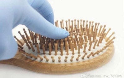 Natural wooden detangling hair brush held by a hand with white bristles