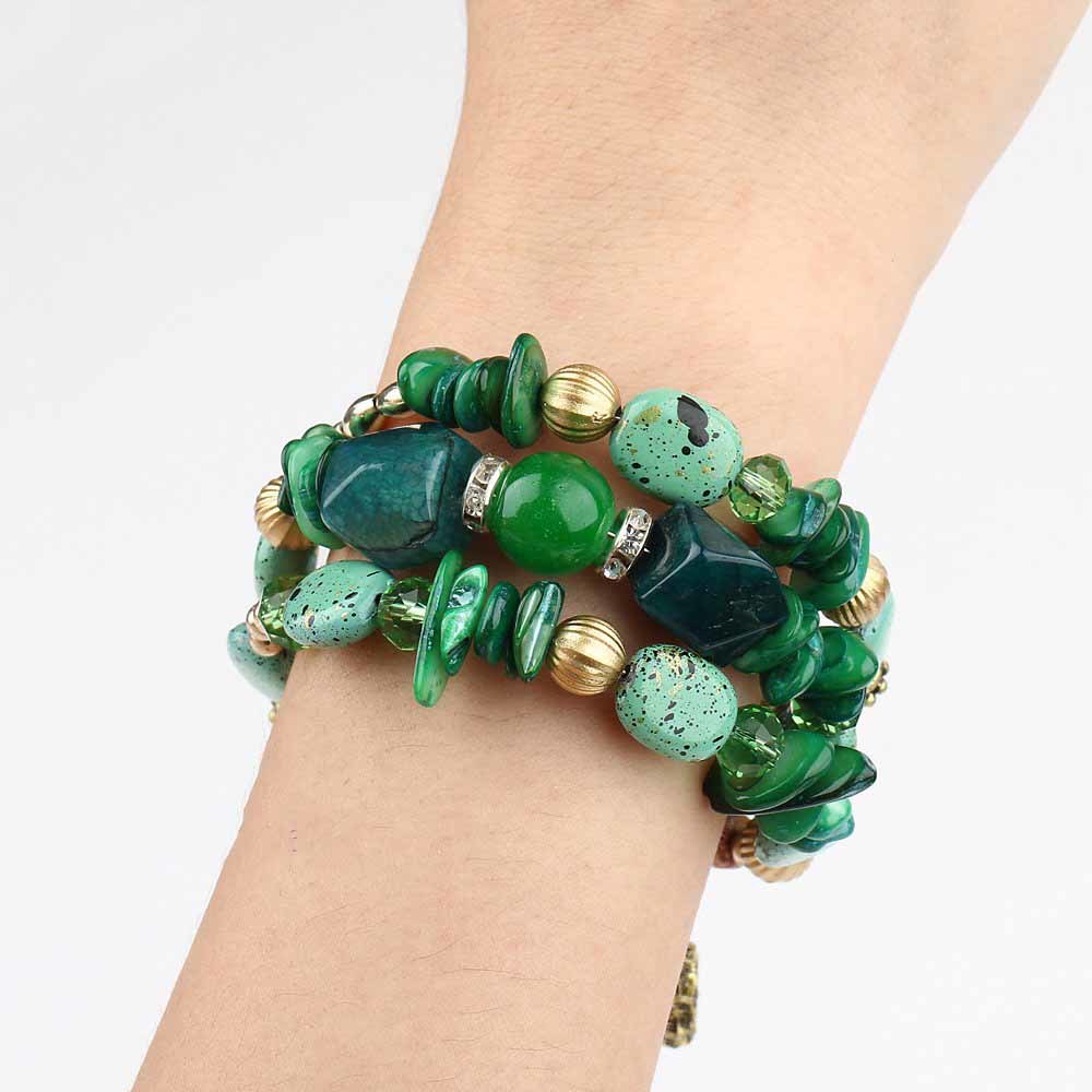 Green boho charm bracelet on wrist with irregular beads, gold rings, and dangling charm.