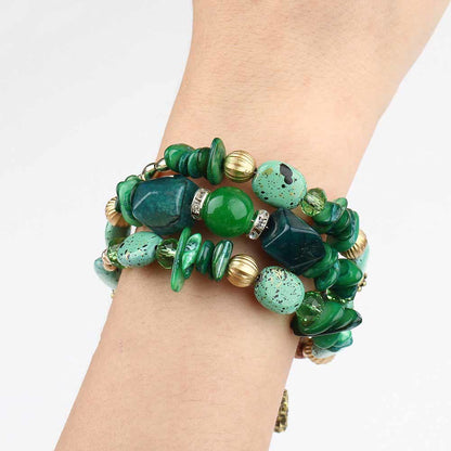 Green boho charm bracelet on wrist with irregular beads, gold rings, and dangling charm.