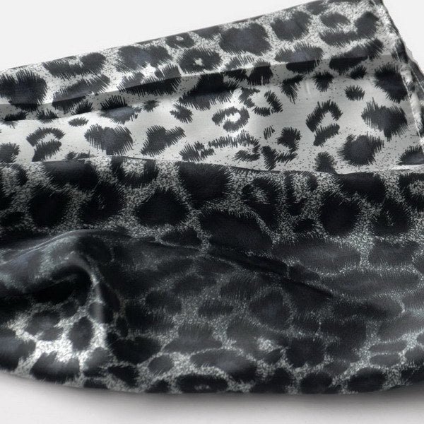 Close-up leopard-print silk scarf fabric with black spots on a light base