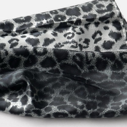 Close-up leopard-print silk scarf fabric with black spots on a light base