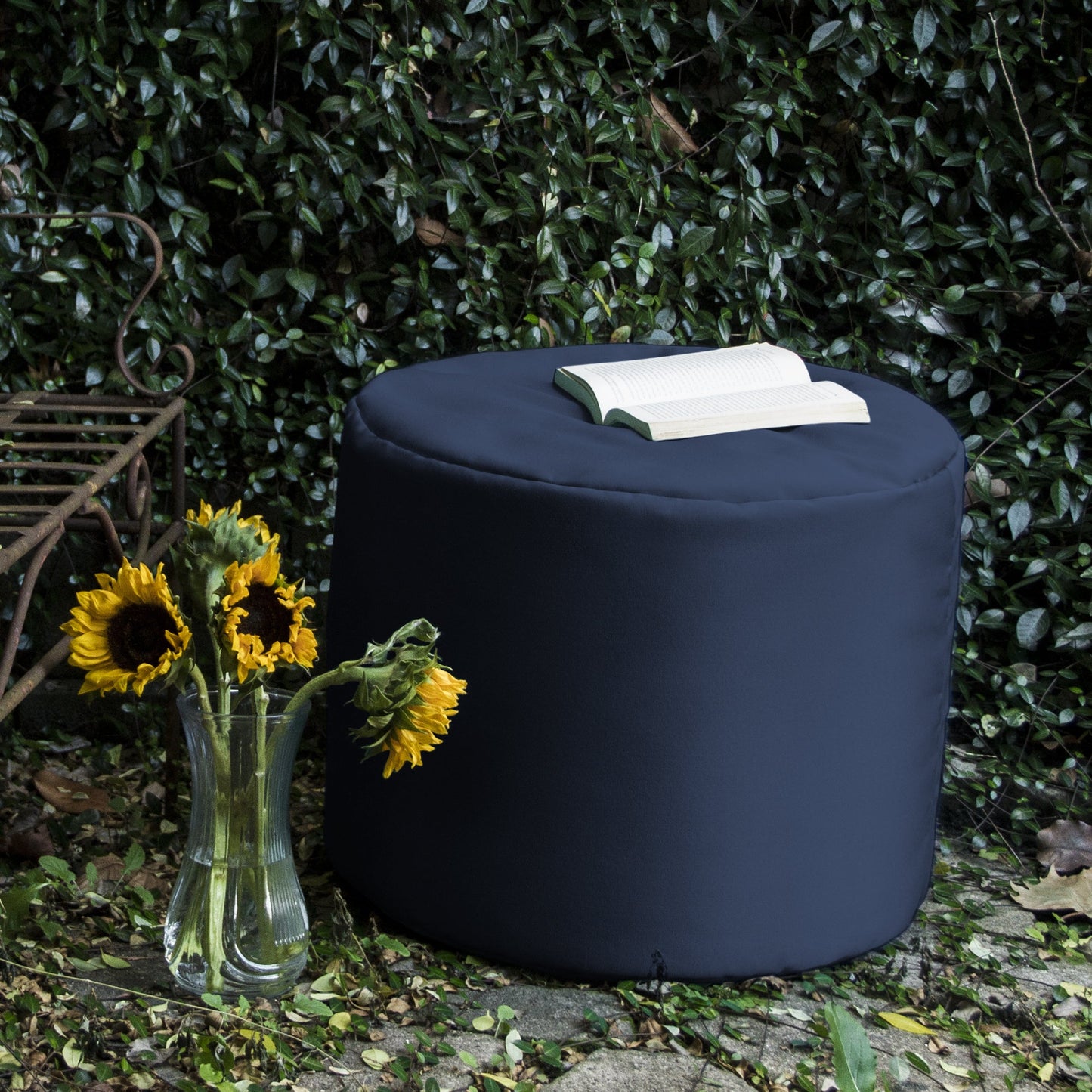 Navy round outdoor ottoman with cushioned top, with a book on top