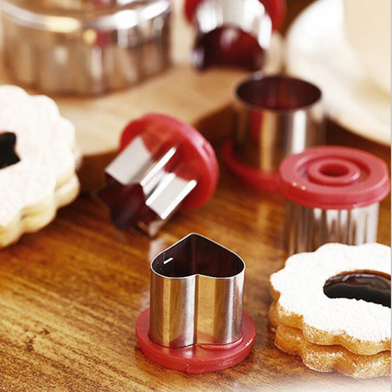 Red and stainless cookie cutters with biscuit shapes on a wooden prep surface