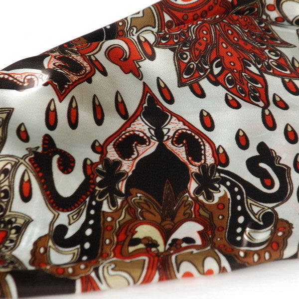 Paisley scarf fabric close-up with ornate red and cream motifs on dark brown