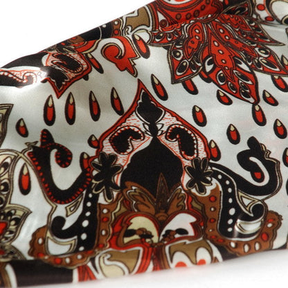 Paisley scarf fabric close-up with ornate red and cream motifs on dark brown
