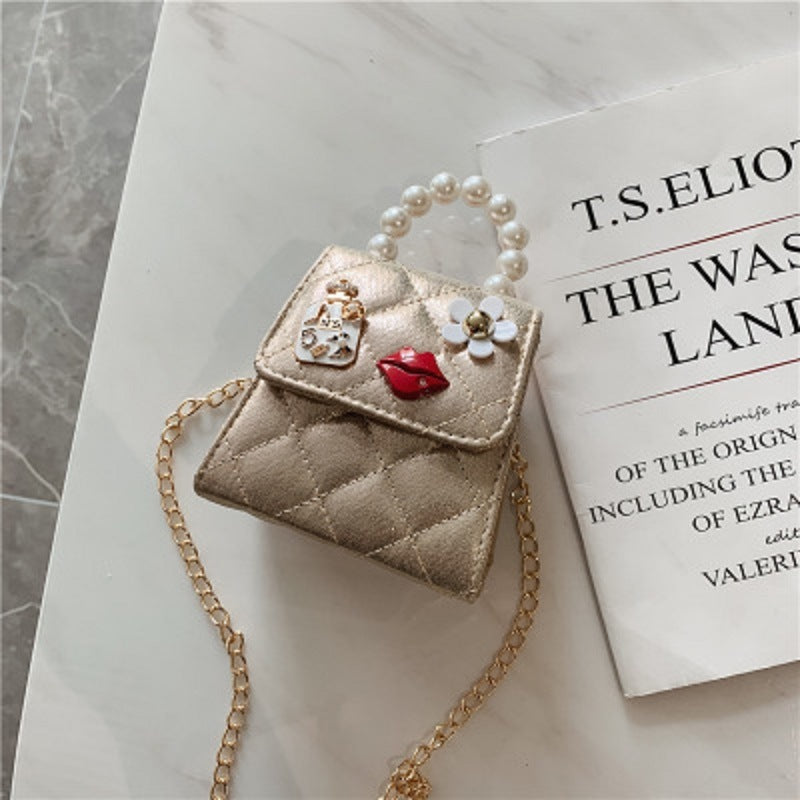 Beige mini quilted crossbody bag with pearl handle, flower charm, and red accent patch