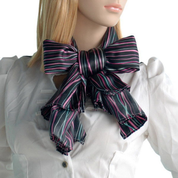 Striped silk scarf tied in a large bow with frayed ends, dark base and pink/teal stripes.