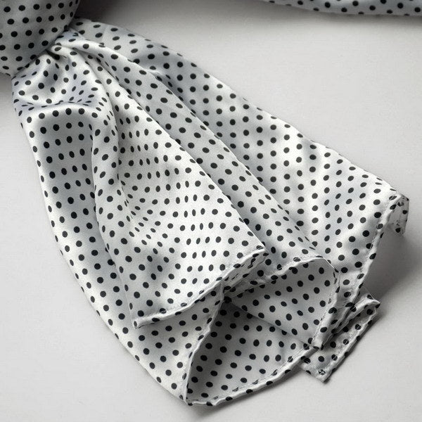 White polka-dot silk scarf close-up showing folded fabric and black dot pattern