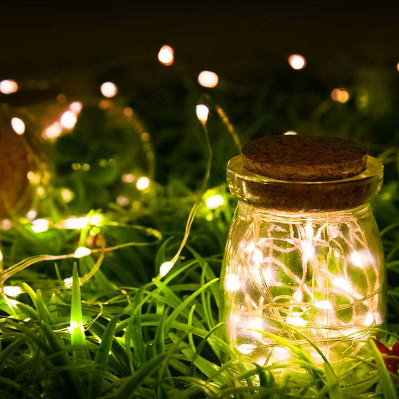 Glass jar filled with warm white fairy lights glowing in green grass