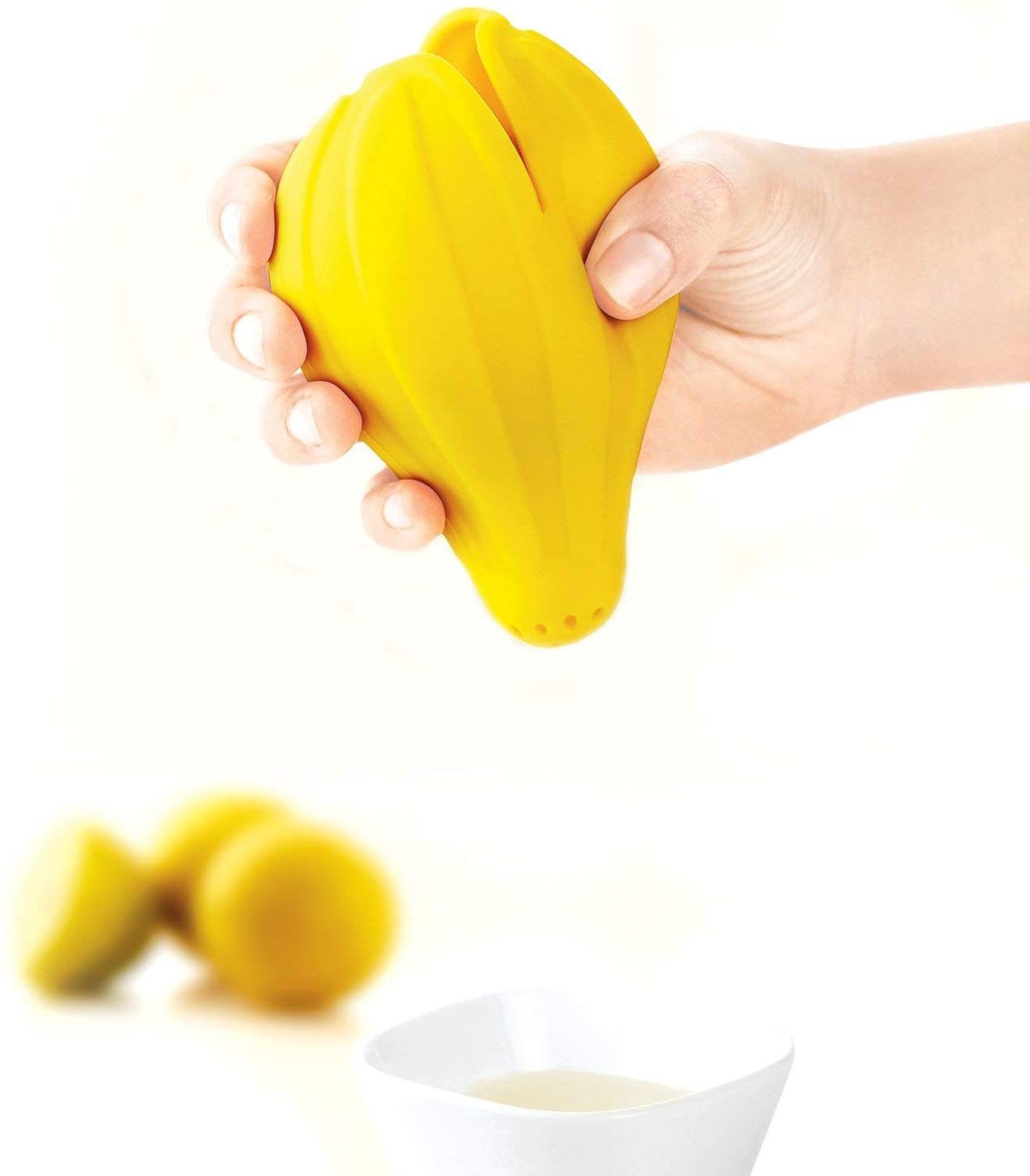 Yellow silicone citrus juicer press being squeezed, juice dripping into cup
