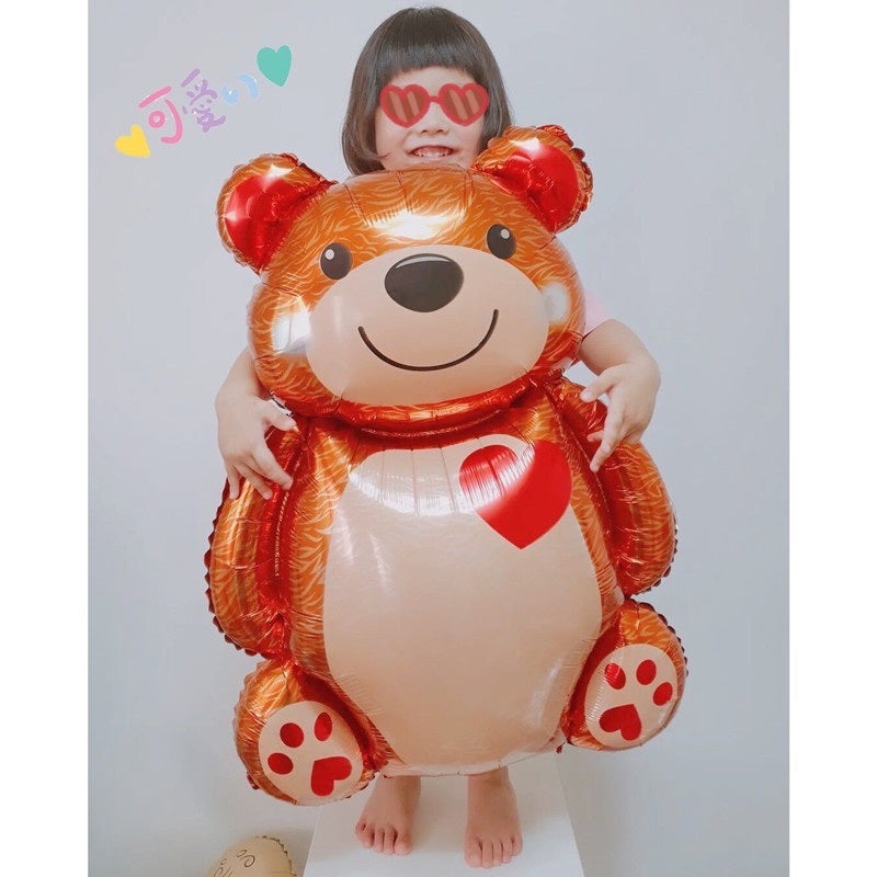 Brown bear foil balloon with red heart, held by two hands