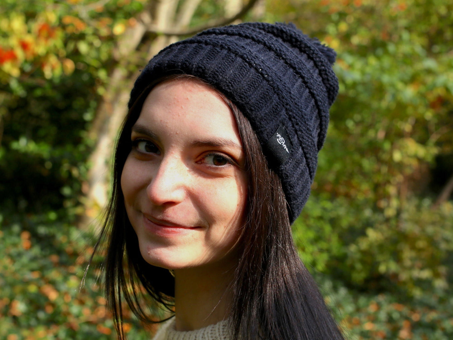 Black cable knit beanie with pom-pom on model, ribbed brim