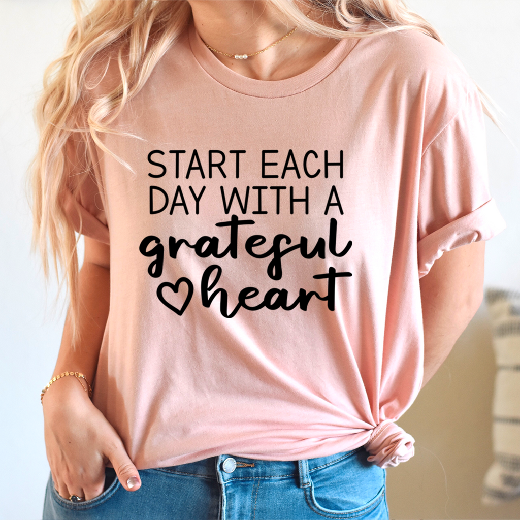 Peach-pink crewneck graphic T-shirt with black 'Start each day' lettering