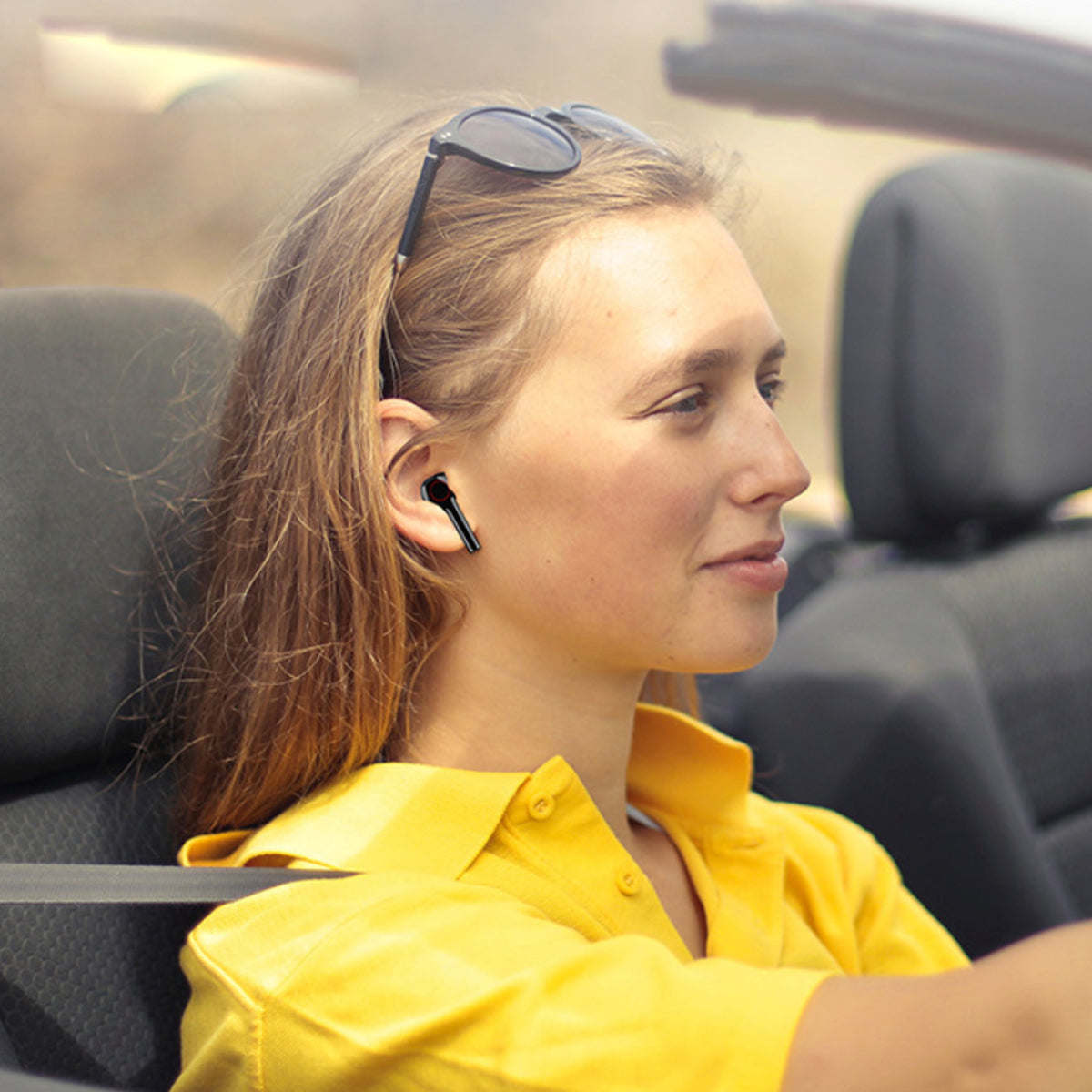 Black wireless Bluetooth earbuds worn in-ear by woman in yellow shirt