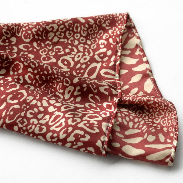 Red and ivory leopard print silk scarf close-up, folded with stitched edge.