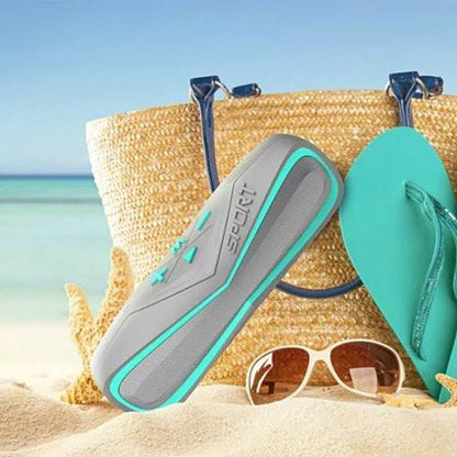 Waterproof Bluetooth speaker with gray body and teal trim near beach items