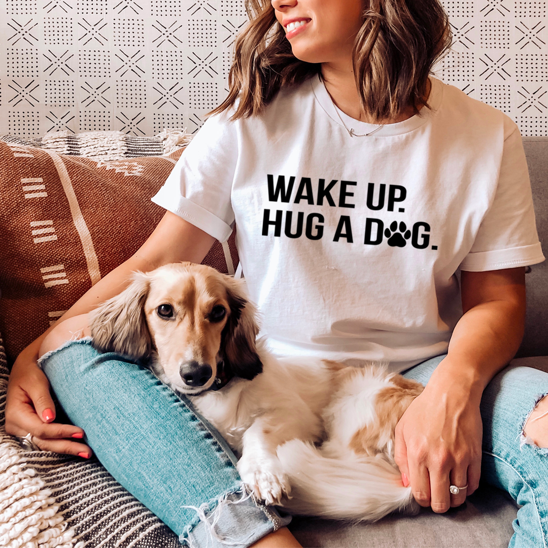 White crewneck t-shirt with bold "WAKE UP. HUG A DOG" paw print graphic, short sleeves