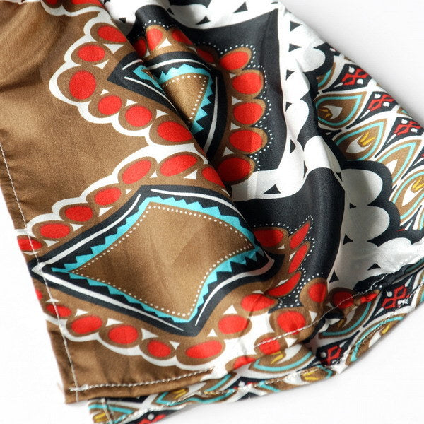 Close-up of patterned scarf fabric with brown base, red circles, teal accents