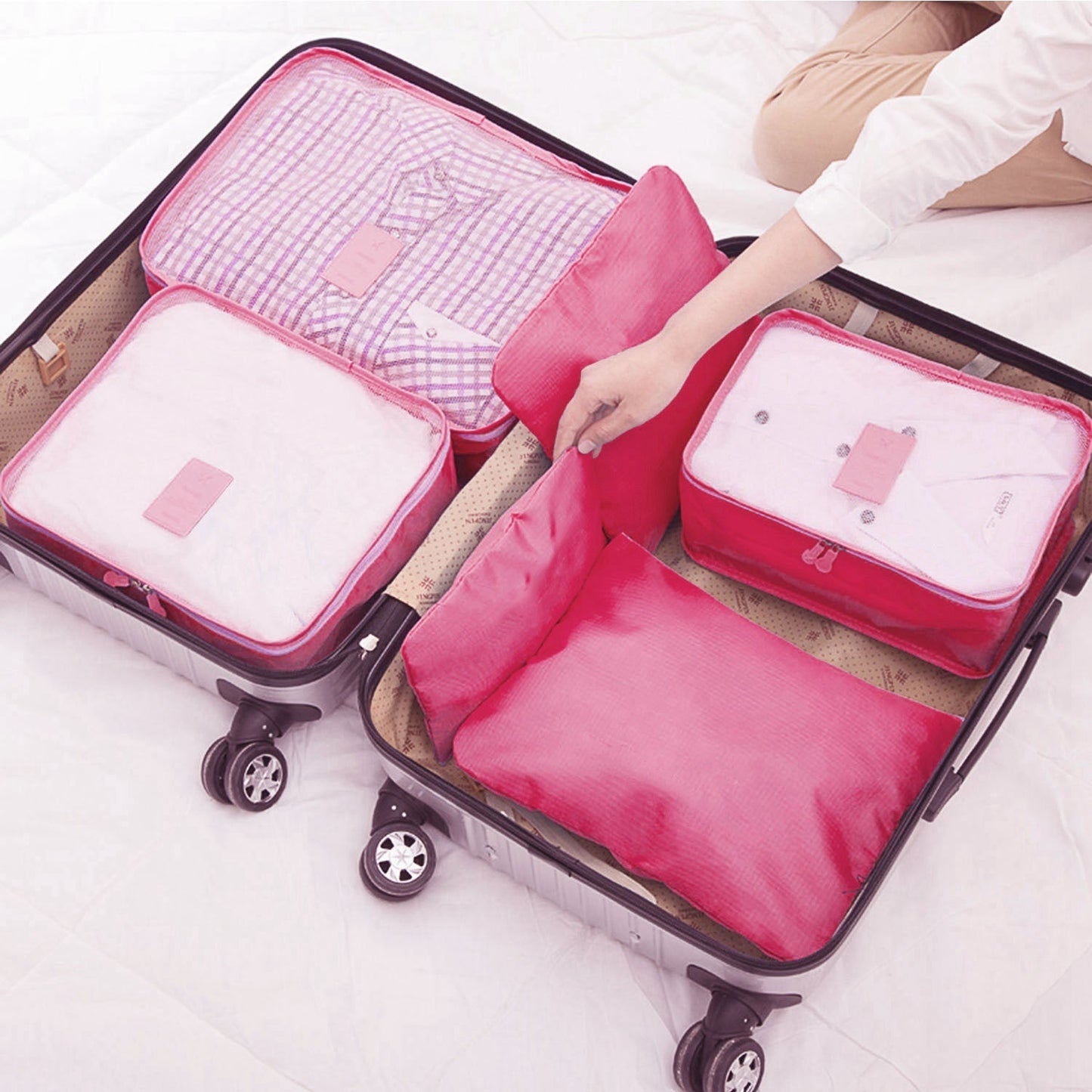 Pink packing cubes and zip pouches in an open rolling suitcase with wheels