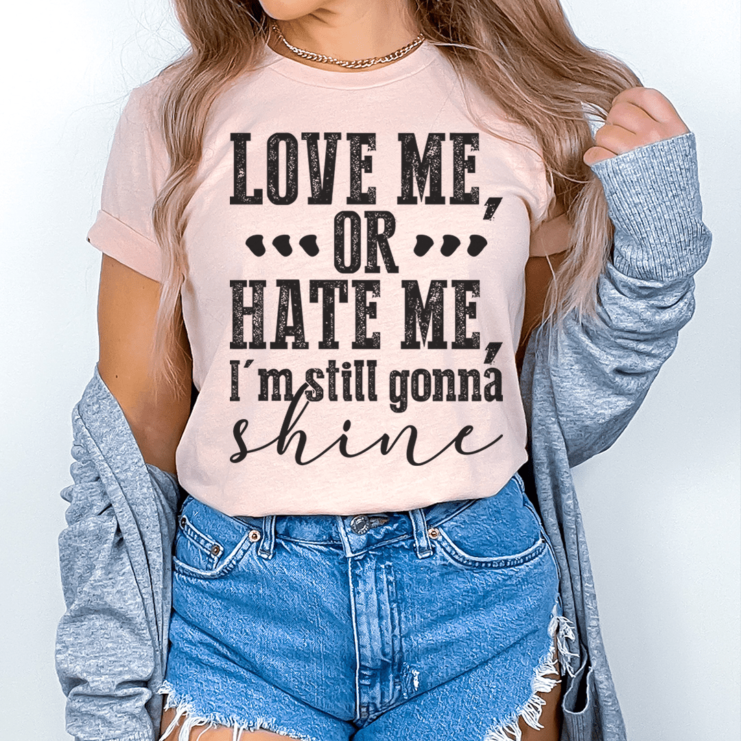 Pink T-shirt worn by model with “LOVE ME, OR HATE ME” graphic and “shine” script