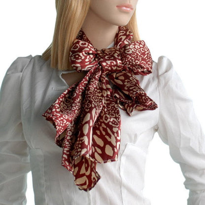 Red and ivory leopard print silk scarf knotted bow at collar on model.