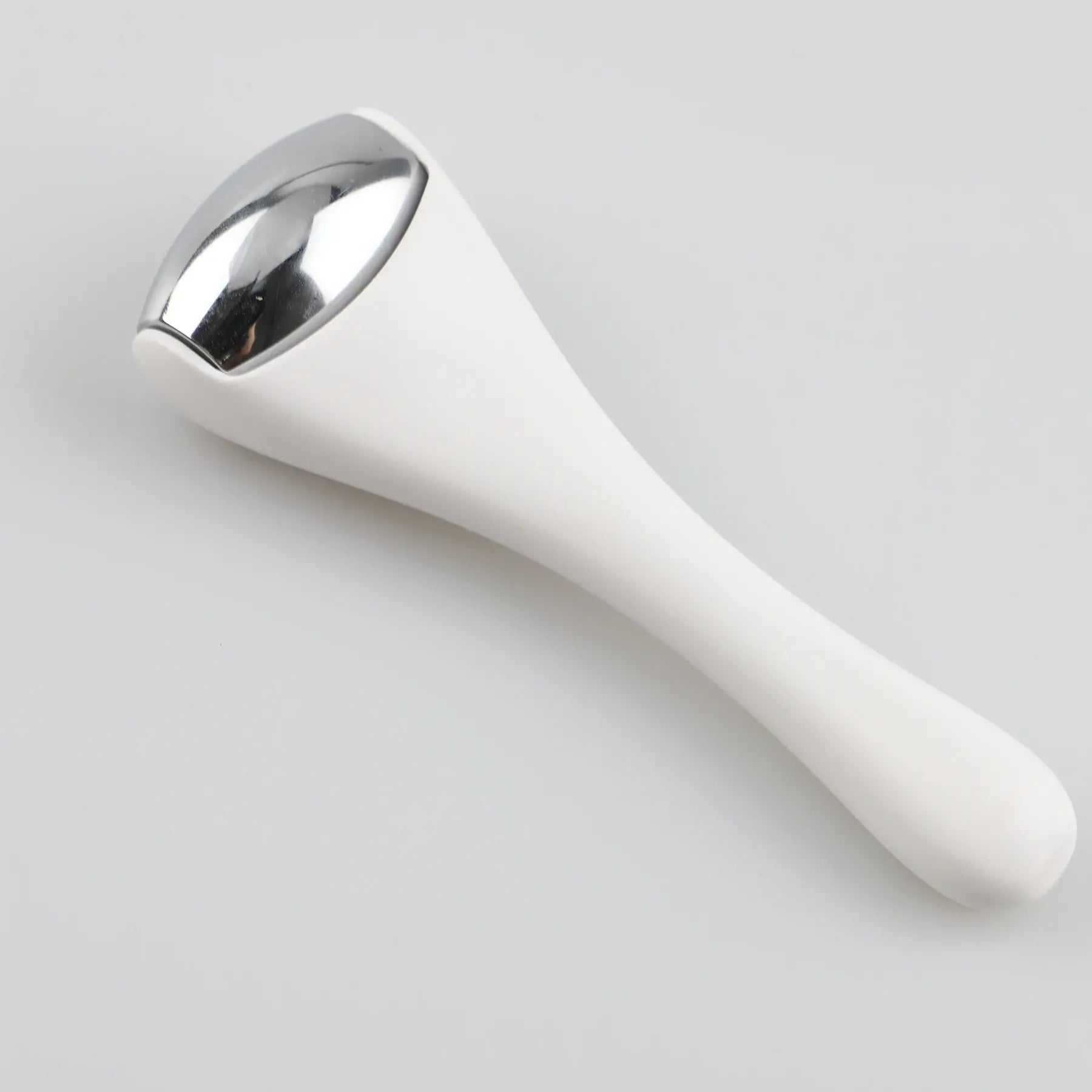 Ice roller massager on its side with white handle and silver roller head