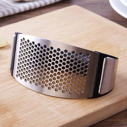 Stainless steel garlic press with black handles and perforated plate on a wooden board