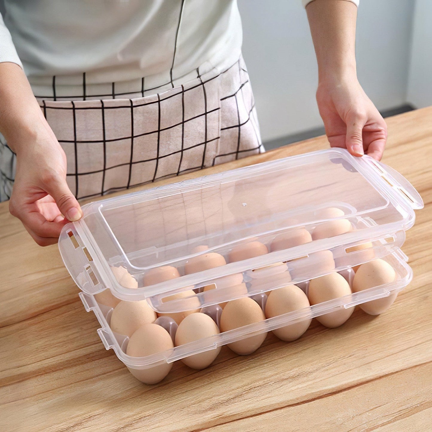 Hand placing a clear-lidded plastic egg storage bin on a wooden table