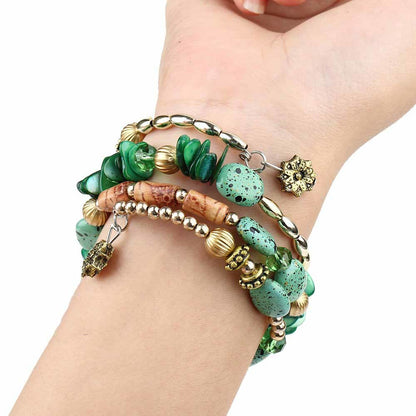 Green boho charm bracelet on wrist with glassy green beads, wood beads, and gold chain charms.