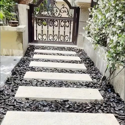 Polished black river rocks along a walkway with smooth stones and white stepping slabs