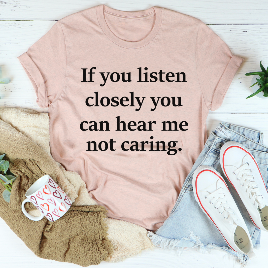Light pink short-sleeve T-shirt with black slogan text: "can hear me not caring"