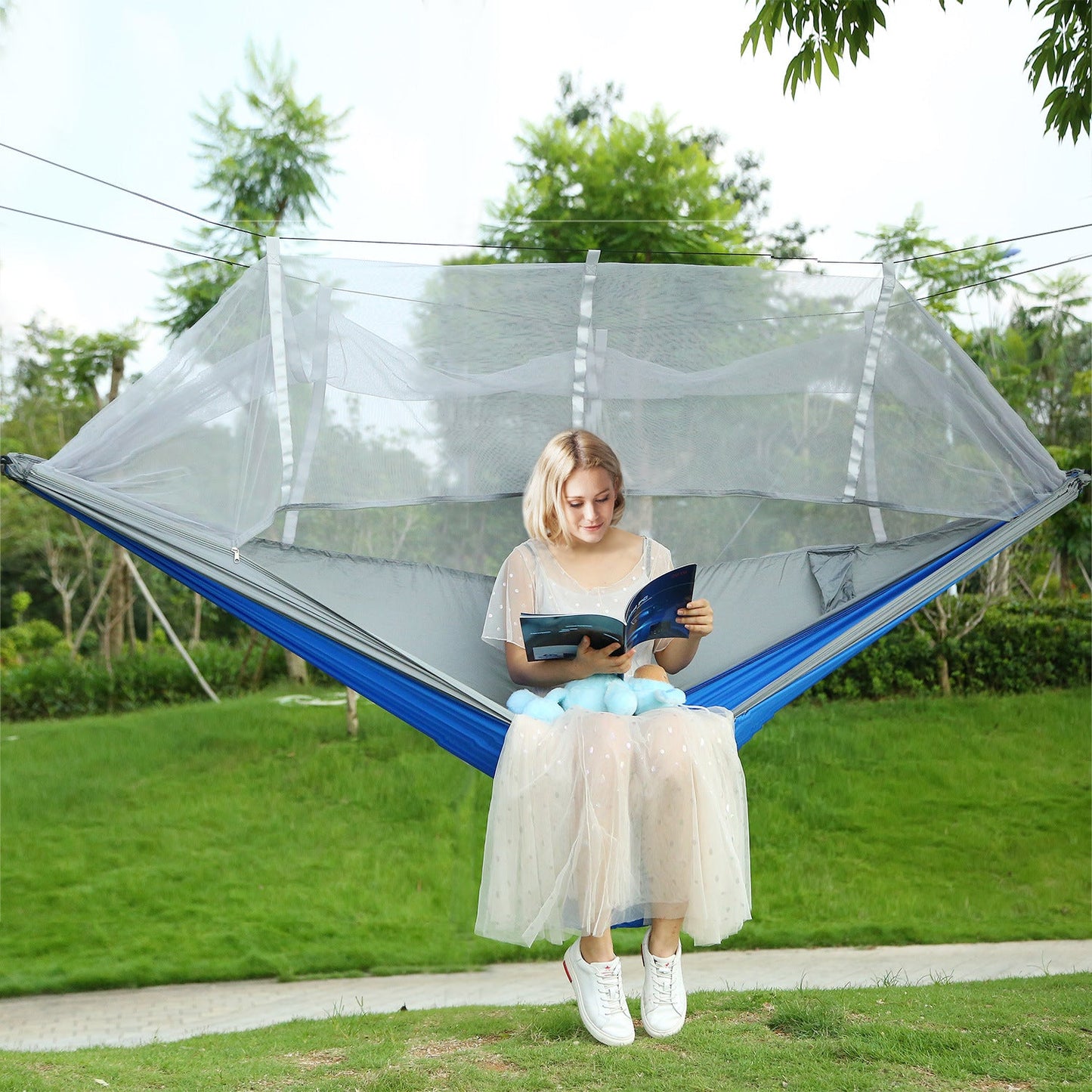 Mosquito-net hammock swing with blue base and clear mesh enclosure, person sitting reading