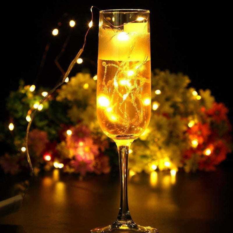 Solar string lights glowing inside a tall glass goblet-shaped lamp on outdoor walkway.