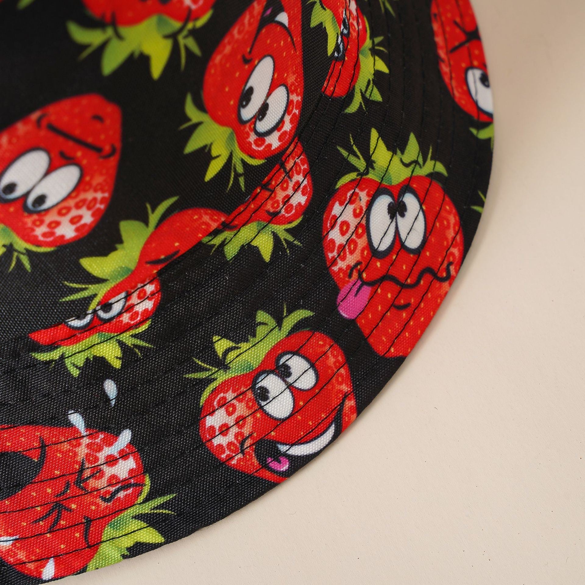 Black cartoon strawberry bucket hat with wide brim, character faces pattern