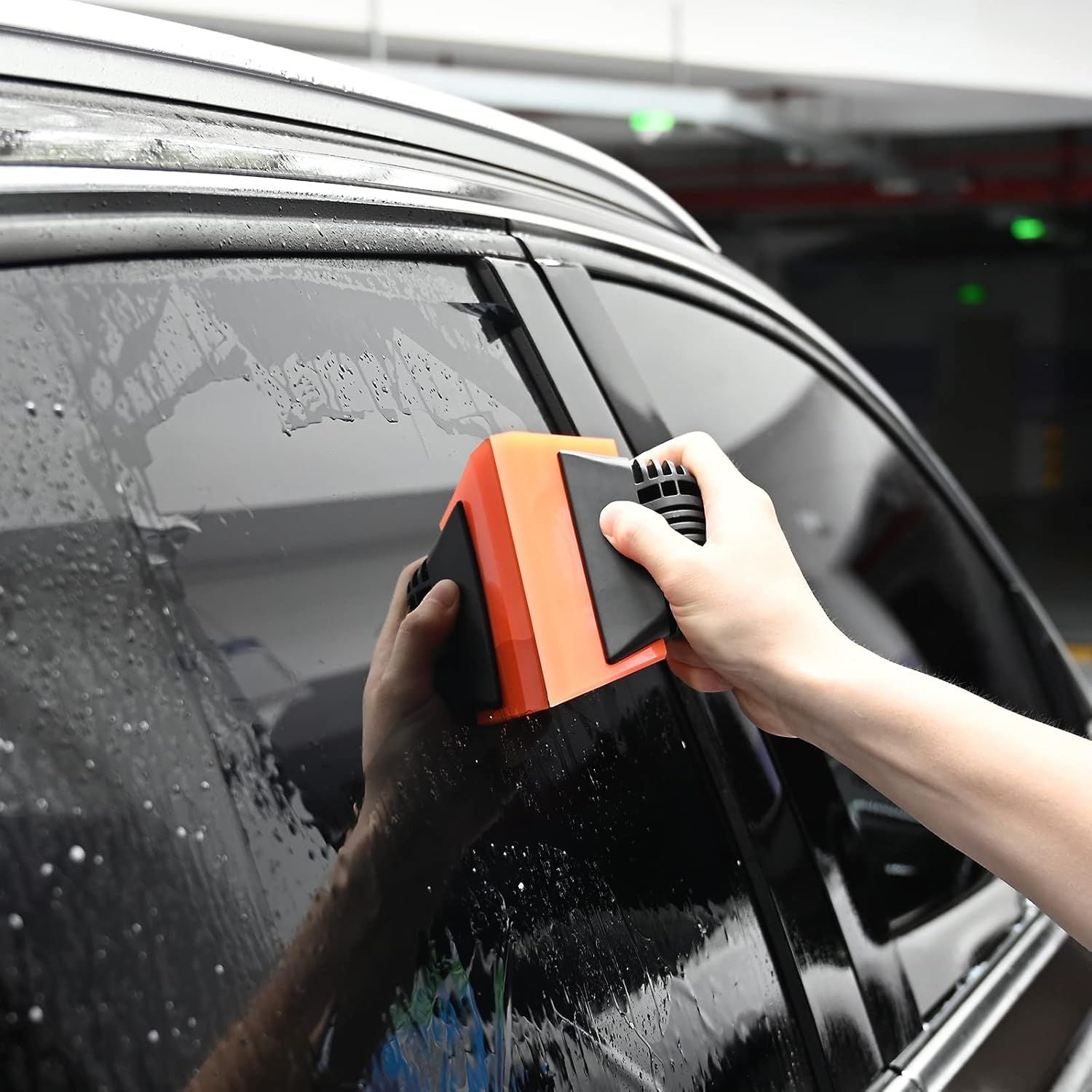 Hand using orange-and-blue window squeegee to remove water from car windshield
