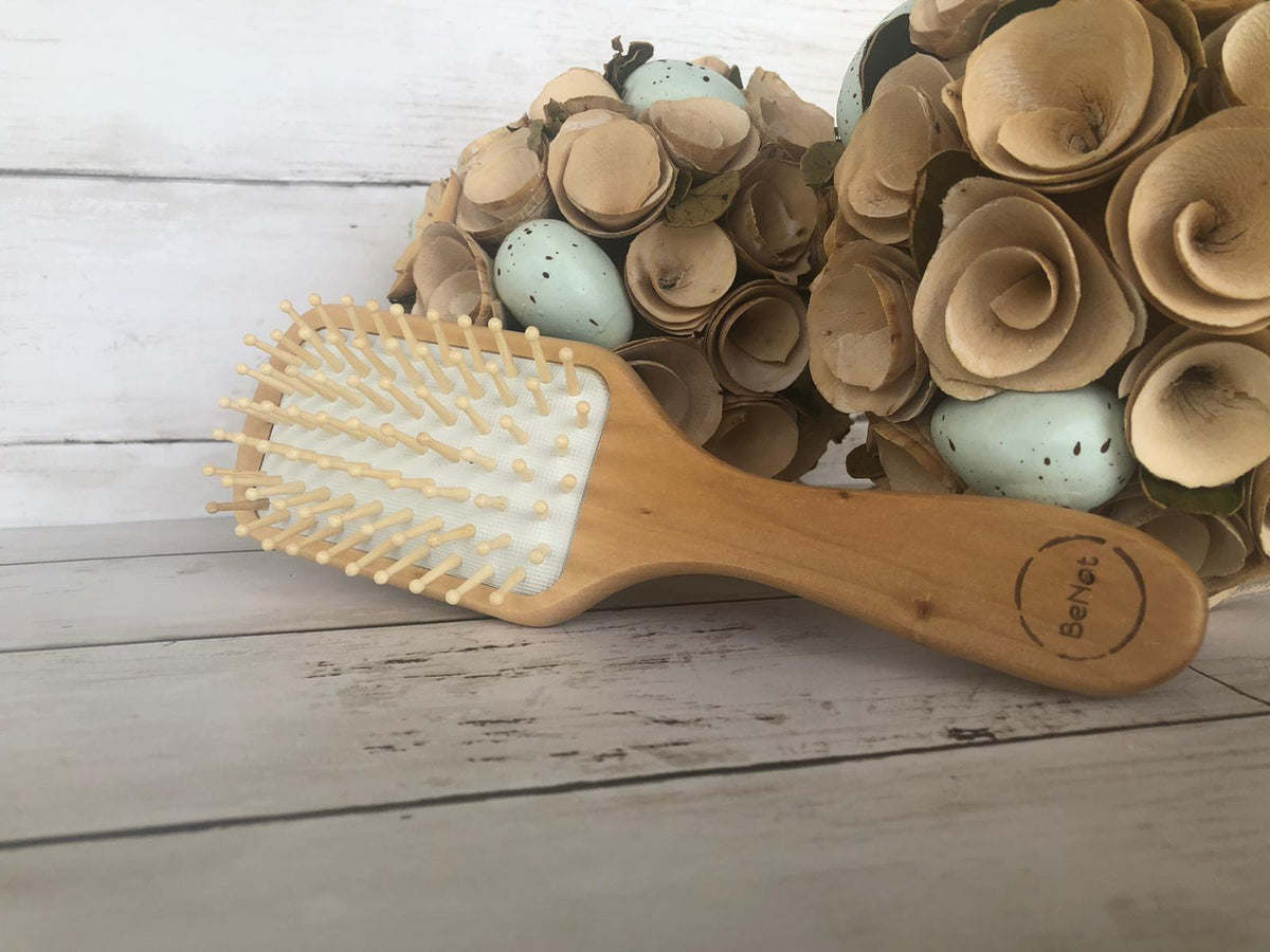 Natural wooden detangling hair brush lying on a surface with white bristles