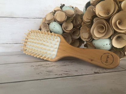 Natural wooden detangling hair brush lying on a surface with white bristles