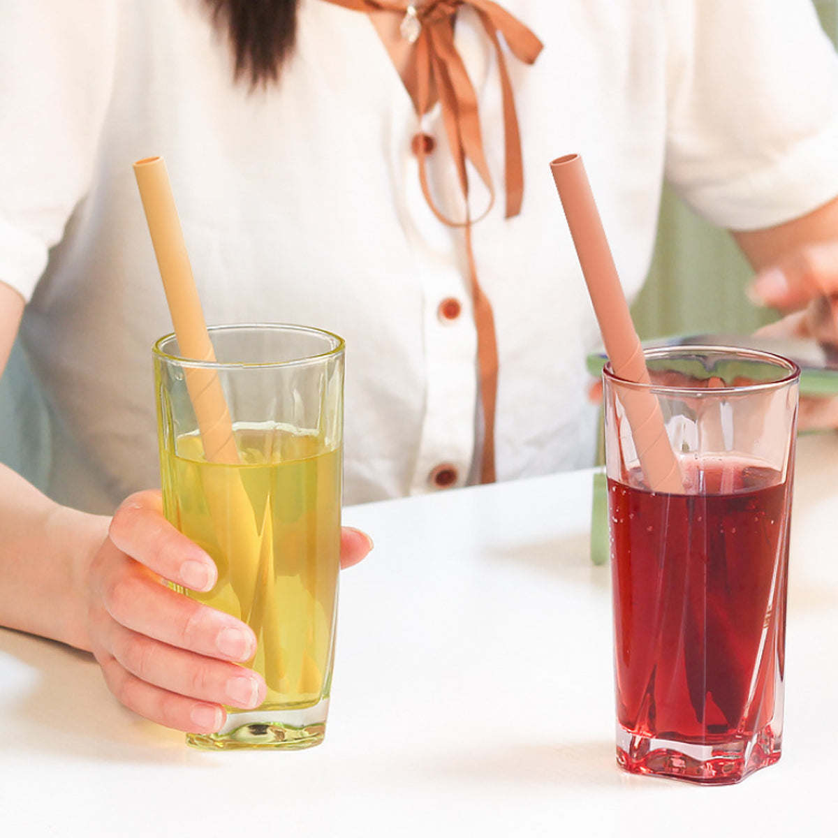 Reusable silicone straws in yellow and red drinks held by a person