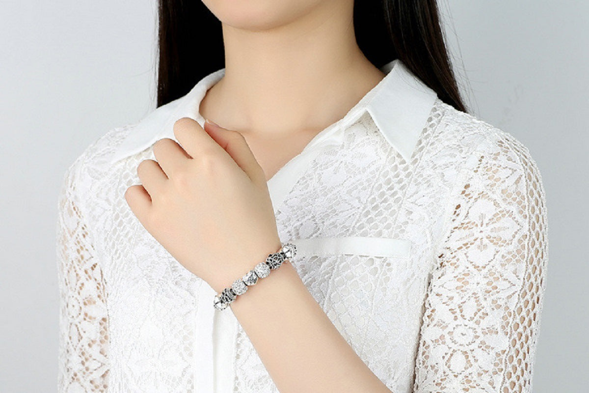 Silver-tone charm bracelet worn on wrist with beaded links and heart charm