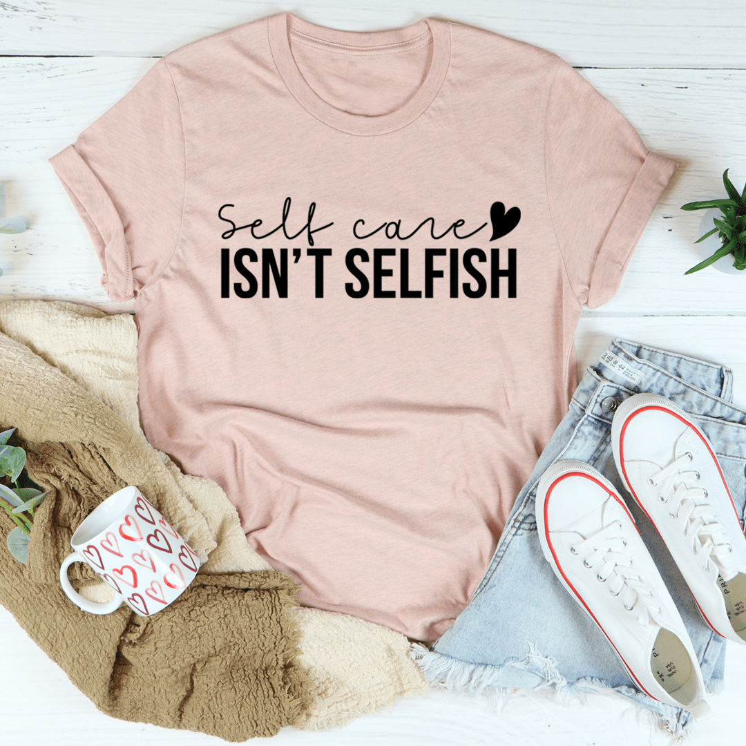 Light mauve/pink T-shirt with “Self care isn’t selfish” text graphic, crew neck